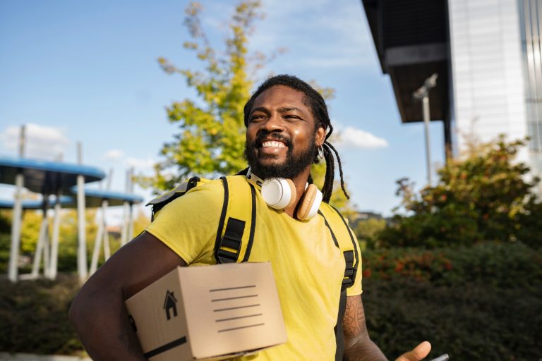 handsome brazilian with dreadlocks delivery man with a box, with headphones smiling around the city