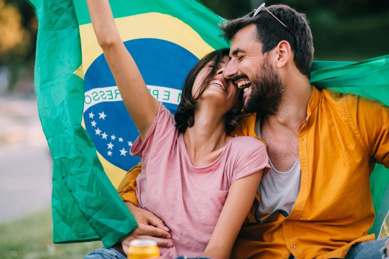 Young couple dancing at a festival in the park with a Brazil flag